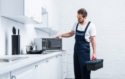 homem adulto faz-tudo com caixa de ferramentas verificando forno micro-ondas na cozinha