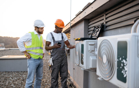 Repairmen with multimeter fixing air conditioner on rooftop